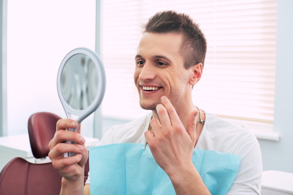 Patient with straight teeth smiling in orthodontist's mirror