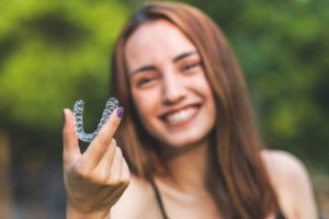 a patient smiling and holding their Invisalign aligner