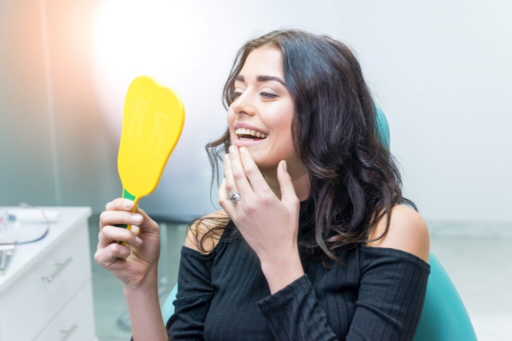 Smiling woman looking at straight teeth in mirror